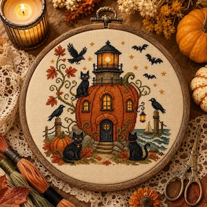 Puede incluir: Un bastidor de bordado circular con un diseño de punto de cruz de un faro con forma de calabaza. La escena incluye gatos negros, cuervos, murciélagos y hojas de otoño sobre tela color crema, en un marco de madera oscura con colgador.