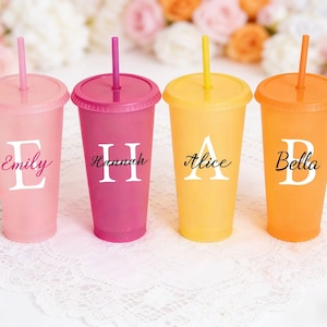 Könnte beinhalten: Vier bunte Plastikbecher mit Deckel und Strohhalm. Jeder Becher hat eine andere Farbe: Rosa, Magenta, Gelb und Orange. Jeder Becher hat einen Namen aufgedruckt: Emily, Hannah, Alice und Bella.