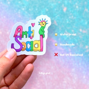 Könnte beinhalten: Ein farbenfroher Aufkleber mit dem Text "Anti Social" in Regenbogenfarben. Eine Cartoonfigur sitzt auf einer rosa Stange. Der Aufkleber ist wasserfest und handgefertigt.