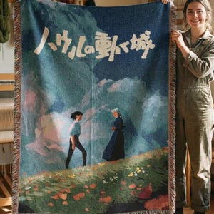 Pode incluir: Um cobertor tecido com uma cena de um filme de anima&ccedil;&atilde;o japon&ecirc;s. O cobertor tem um fundo azul com um desenho de paisagem e texto japon&ecirc;s. O cobertor tem franjas nas bordas e &eacute; feito sob encomenda.