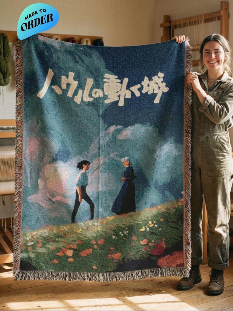 Pode incluir: Um cobertor tecido com uma cena de um filme de anima&ccedil;&atilde;o japon&ecirc;s. O cobertor tem um fundo azul com um desenho de paisagem e texto japon&ecirc;s. O cobertor tem franjas nas bordas e &eacute; feito sob encomenda.