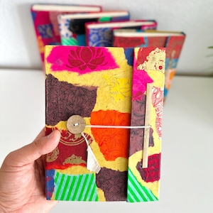 Pode incluir: Um diário retangular com uma capa de patchwork vibrante em seções amarelas, vermelhas, laranjas e verdes. A capa apresenta vários padrões florais e geométricos, um fecho de botão de madeira circular e um cordão branco fino.