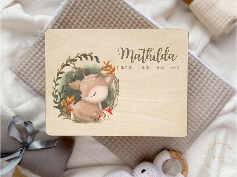 以下が含まれることがあります： 木製のプレートに「Mathilda」という名前がエレガントな筆記体で書かれています。 葉に囲まれた子鹿の水彩イラストが特徴です。 プレートには、20.07.2025、21:45、51cm、3845gの誕生日の詳細が含まれています。