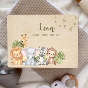 以下が含まれることがあります： 「Leon」の名前と出生詳細が書かれた木製プレート。ライオン、キリン、ゾウ、シマウマ、サルのイラストが特徴です。プレートには日付、時間、長さ（52cm）、重さ（3840g）が記載されています。