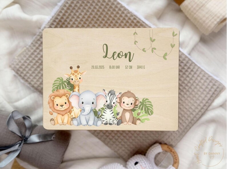 以下が含まれることがあります： 「Leon」の名前と出生詳細が書かれた木製プレート。ライオン、キリン、ゾウ、シマウマ、サルのイラストが特徴です。プレートには日付、時間、長さ（52cm）、重さ（3840g）が記載されています。