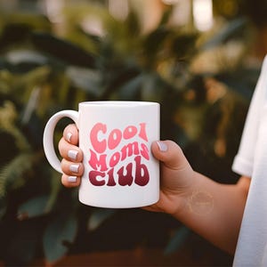 May include: A white ceramic mug with a black handle and the text "But First, Coffee" in a black, handwritten-style font. The mug is on a white surface.