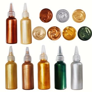 May include: A selection of metallic paint bottles in shades of gold, silver, bronze, and green. The image also displays paint swatches, showcasing the colour and sheen. The bottles have clear nozzles for accurate application.