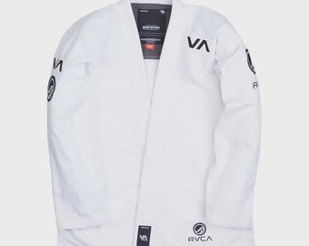 May include: A white martial arts gi with black logos and text. The gi features the brand name "RVCA" and "VA" on the front and sleeves. The gi has a collar and is designed for martial arts training.