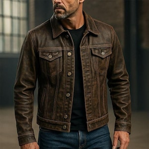 Könnte beinhalten: Braune Lederjacke mit klassischem Design. Die Jacke hat eine Knopfleiste, zwei Brusttaschen und einen Kragen. Die Jacke wird mit einem schwarzen Hemd und einer blauen Jeans getragen.