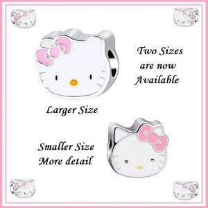 Peut inclure: Deux breloques Hello Kitty argentées de différentes tailles. Les breloques présentent un visage blanc avec un nœud rose, un nez jaune et des yeux noirs. Le texte sur l'image indique "Two Sizes are now Available", "Larger Size" et "Smaller Size More detail".