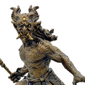 May include: A bronze-colored statue of a mythical creature with horns, a third eye, and a fierce expression. The creature is holding a staff in its right hand and is standing on a circular base.