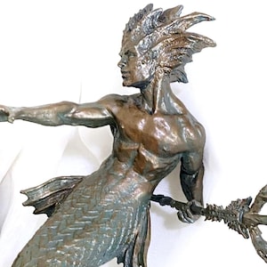 May include: Bronze sculpture of a merman holding a trident. The merman has a fish tail and is standing on a seashell. The sculpture is on a wooden surface.