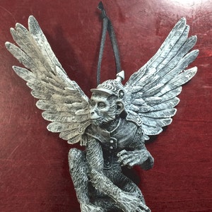 May include: A white and gray winged monkey figurine wearing a military helmet. The monkey is perched on a branch with its wings spread out.
