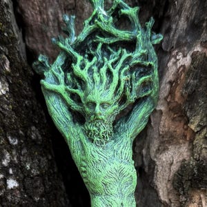 May include: Green tree spirit statue with a human-like body and branches for hair. The statue is standing on a tree stump.