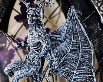 May include: A silver-colored skeletal creature with antlers and wings hangs from a black cord inside a decorative metal lantern. The creature is detailed with a textured surface and appears to be made of metal.