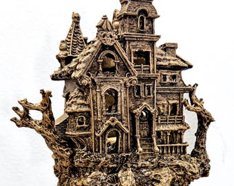 Puede incluir: Una detallada escultura en miniatura de una casa embrujada marrón. La estructura de varios pisos presenta intrincados detalles arquitectónicos, incluyendo torres, balcones y una escalera de caracol que conduce a la casa. La escultura está montada sobre una base oscura y redonda.