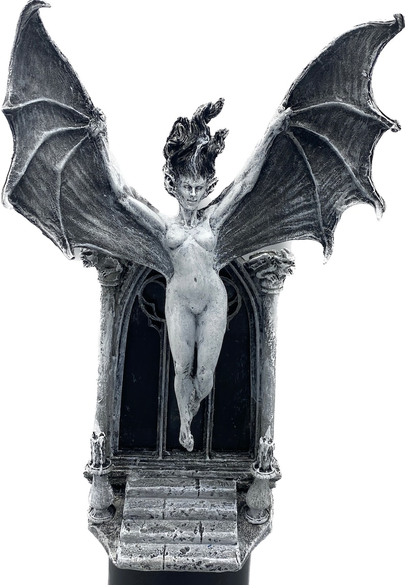 Pode incluir: Uma escultura de uma figura feminina alada branca com um arco g&oacute;tico e velas. A figura est&aacute; nua e tem cabelo comprido e solto. A escultura &eacute; feita de um material branco e tem uma base preta.