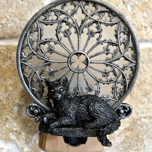 Peut inclure: Une veilleuse en forme de chat noir avec un motif de fen&ecirc;tre gothique argent&eacute;. Le chat est assis sur un rebord avec sa queue enroul&eacute;e autour de son corps. La veilleuse a un interrupteur sur le c&ocirc;t&eacute;.
