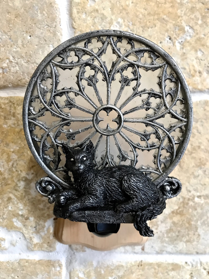 Peut inclure: Une veilleuse en forme de chat noir avec un motif de fen&ecirc;tre gothique argent&eacute;. Le chat est assis sur un rebord avec sa queue enroul&eacute;e autour de son corps. La veilleuse a un interrupteur sur le c&ocirc;t&eacute;.