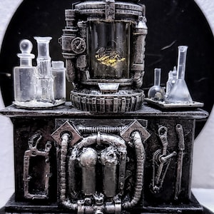 May include: A detailed, steampunk-style laboratory model with a central glass chamber containing a golden object. The model features various glass vials, beakers, and metallic components, all in shades of gray and silver.