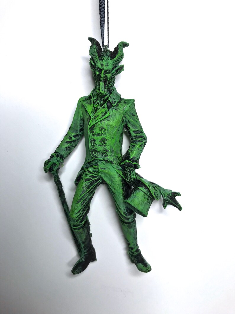 May include: Green, demonic-looking figure ornament with horns, a top hat, and a cane. The figure is wearing a suit and has a long, pointed tongue.