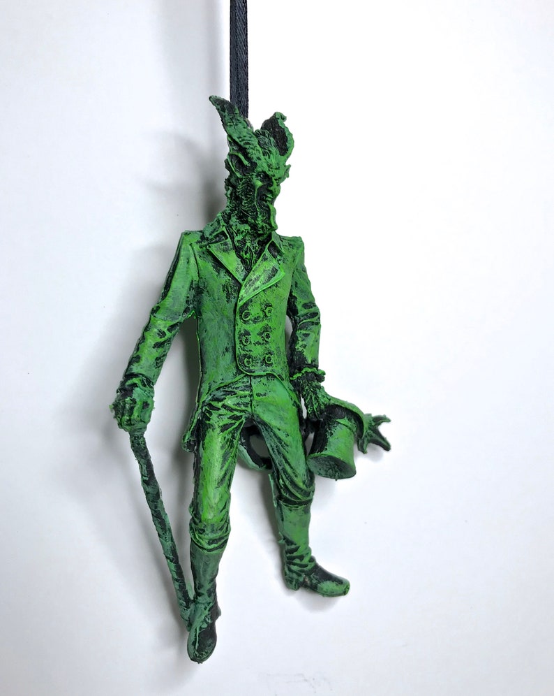 May include: A green figurine of a creature wearing a suit and holding a top hat and a cane. The creature has a long snout and horns.