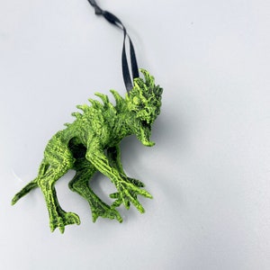 May include: Green monster ornament with a black ribbon for hanging. The monster has sharp teeth and claws.
