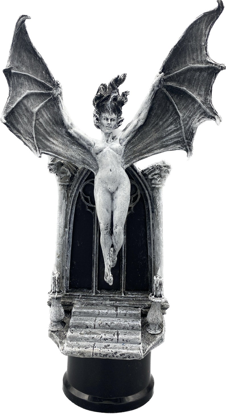 Pode incluir: Uma figurinha esculpida em cinza e branco de uma mulher alada com as asas estendidas, em p&eacute; sobre uma base de pedra com um arco g&oacute;tico. A figurinha &eacute; uma pe&ccedil;a decorativa de estilo g&oacute;tico.