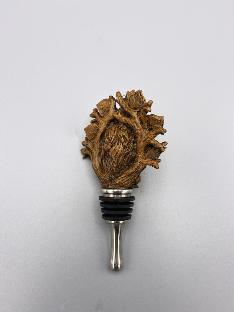 Op de afbeelding: Een houten flessenstop in de vorm van een hart met takken en bladeren. De stop is gemaakt van bruin hout en heeft een zilveren metalen basis.