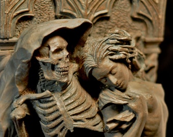 May include: A detailed sculpture of a skeletal figure in a hooded robe embracing a woman. The sculpture is made of a dark brown material and has a gothic aesthetic.