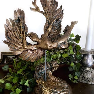 May include: A bronze sculpture of a winged figure with outstretched arms, falling into a wave. The sculpture is mounted on a wooden base.