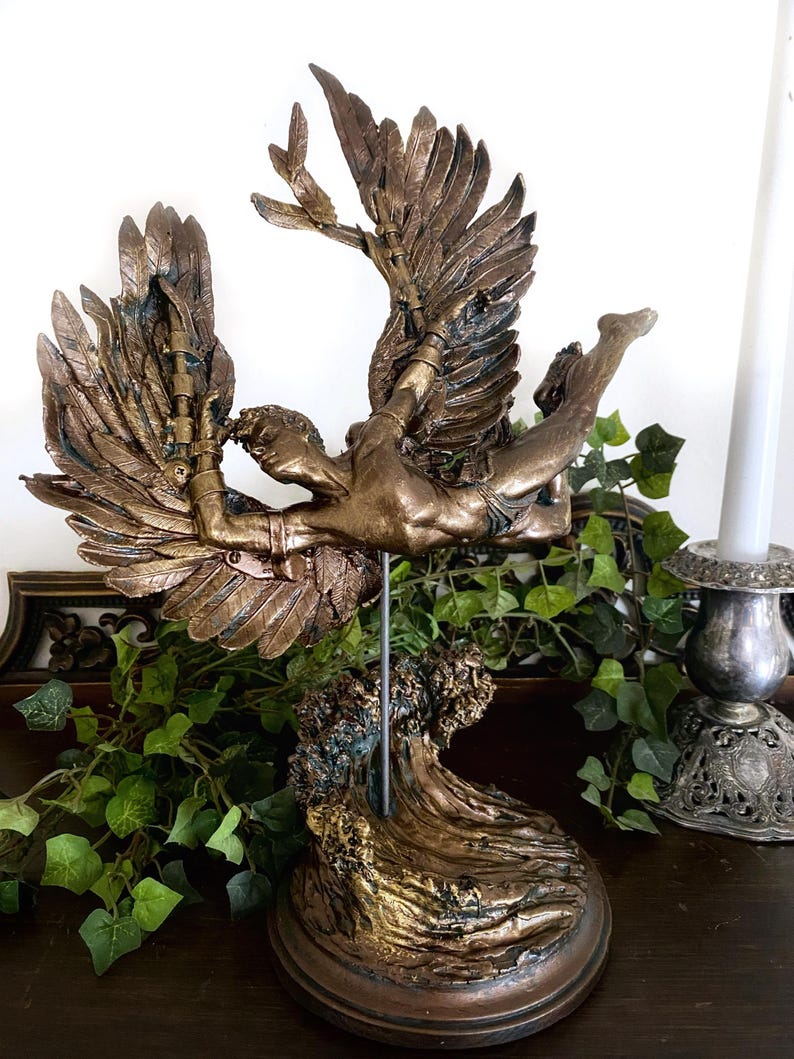 May include: A bronze sculpture of a winged figure with outstretched arms, falling into a wave. The sculpture is mounted on a wooden base.