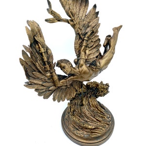 May include: A bronze sculpture of a winged figure with outstretched wings, falling through the air. The figure is depicted with a muscular physique and a determined expression. The sculpture is mounted on a base that resembles a wave.