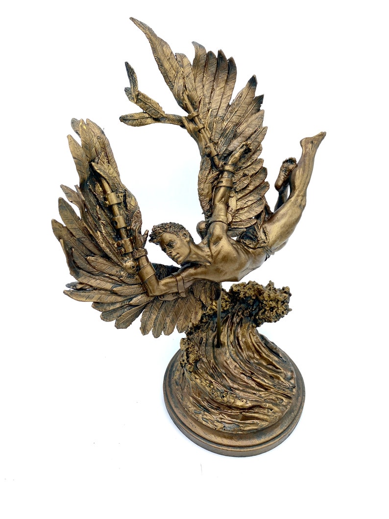 May include: A bronze sculpture of a winged figure with outstretched wings, falling through the air. The figure is depicted with a muscular physique and a determined expression. The sculpture is mounted on a base that resembles a wave.
