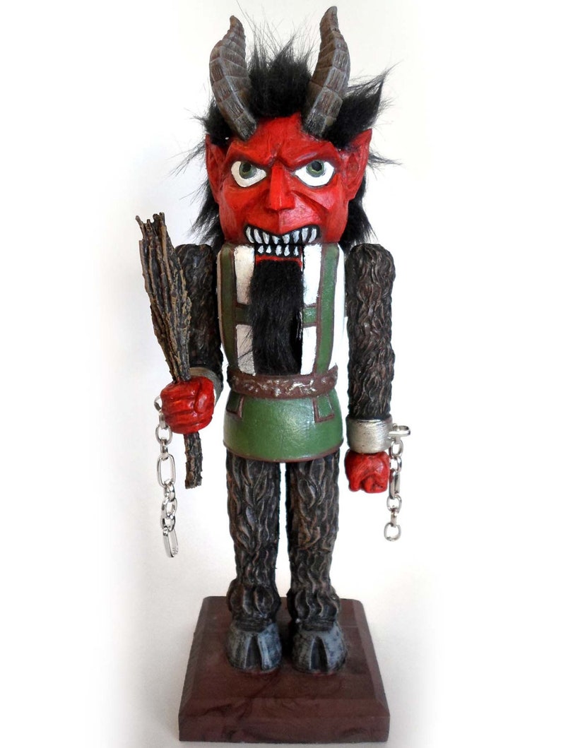 May include: A red and black Christmas nutcracker with horns, a beard, and a green and white outfit. The nutcracker is holding a stick and chains in its hands.