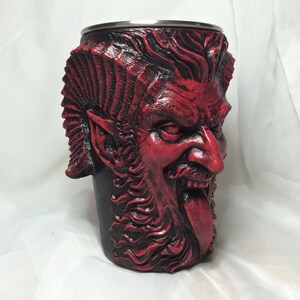 May include: A red and black ceramic mug shaped like a demon's head with horns, a beard, and a tongue sticking out.