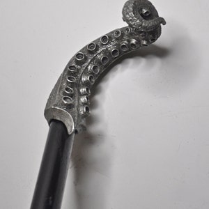 May include: A silver walking stick with an octopus-shaped handle. The handle is curled and has a textured surface.