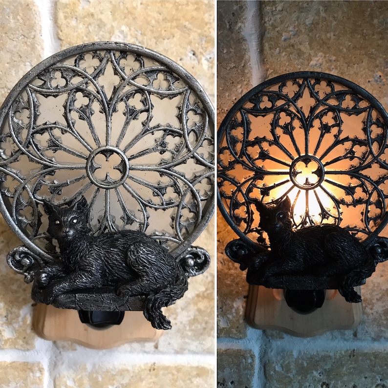 Peut inclure: Une figurine de chat noir est plac&eacute;e &agrave; l'int&eacute;rieur d'une veilleuse en m&eacute;tal d&eacute;corative en forme de fen&ecirc;tre gothique. La veilleuse est branch&eacute;e et allum&eacute;e, projetant une lueur chaude.