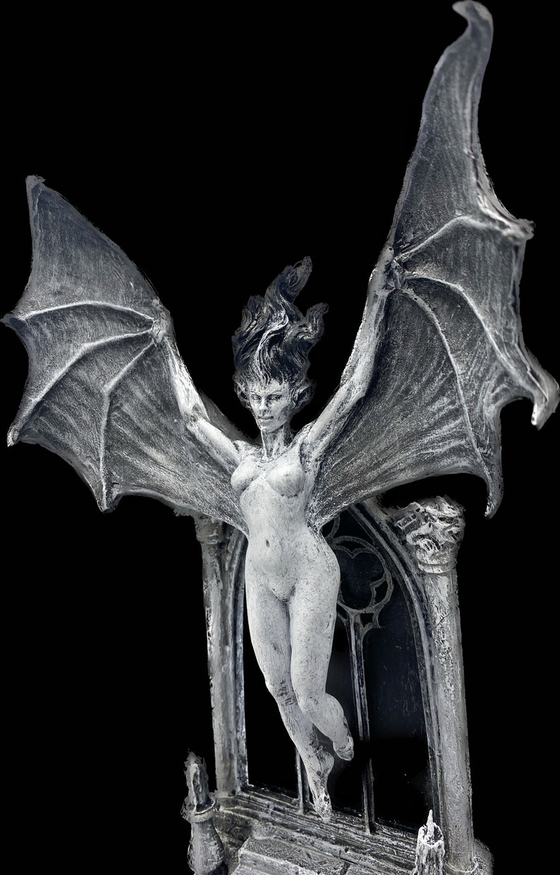 Pode incluir: Uma figura branca esculpida de uma mulher alada com os bra&ccedil;os estendidos, em p&eacute; sobre um pedestal de pedra com um arco g&oacute;tico atr&aacute;s dela.