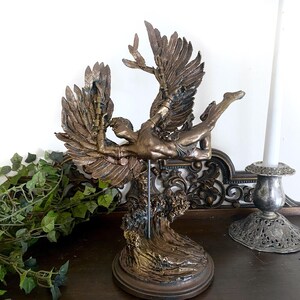 May include: A bronze sculpture of a winged figure with outstretched arms, standing on a base with a wave-like design. The figure is depicted in mid-flight, with its wings spread wide.