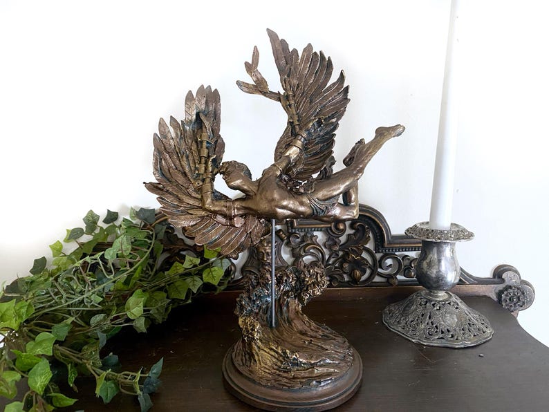May include: A bronze sculpture of a winged figure with outstretched arms, standing on a base with a wave-like design. The figure is depicted in mid-flight, with its wings spread wide.