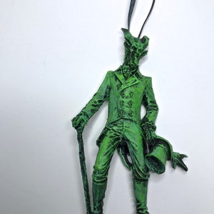 May include: Green, detailed, sculpted figurine of a man in a suit with a top hat and cane. The figurine is a Christmas ornament.