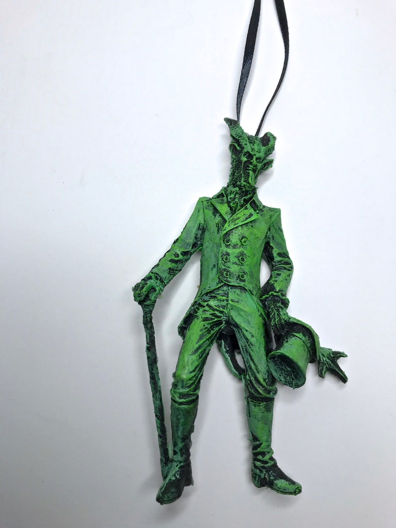 May include: Green, detailed, sculpted figurine of a man in a suit with a top hat and cane. The figurine is a Christmas ornament.
