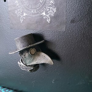 Pu&ograve; includere: Una maschera di medico della peste color argento con un cappello nero e una lunga sciarpa fluente. La maschera ha un becco grande e rotondo e un piccolo foro rotondo per gli occhi.