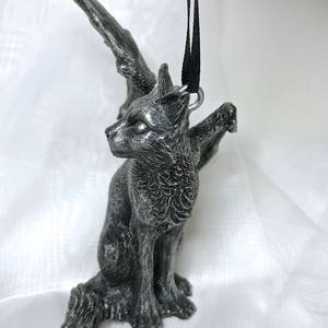 May include: A silver-colored winged cat figurine ornament with a black ribbon attached to a loop on its back.