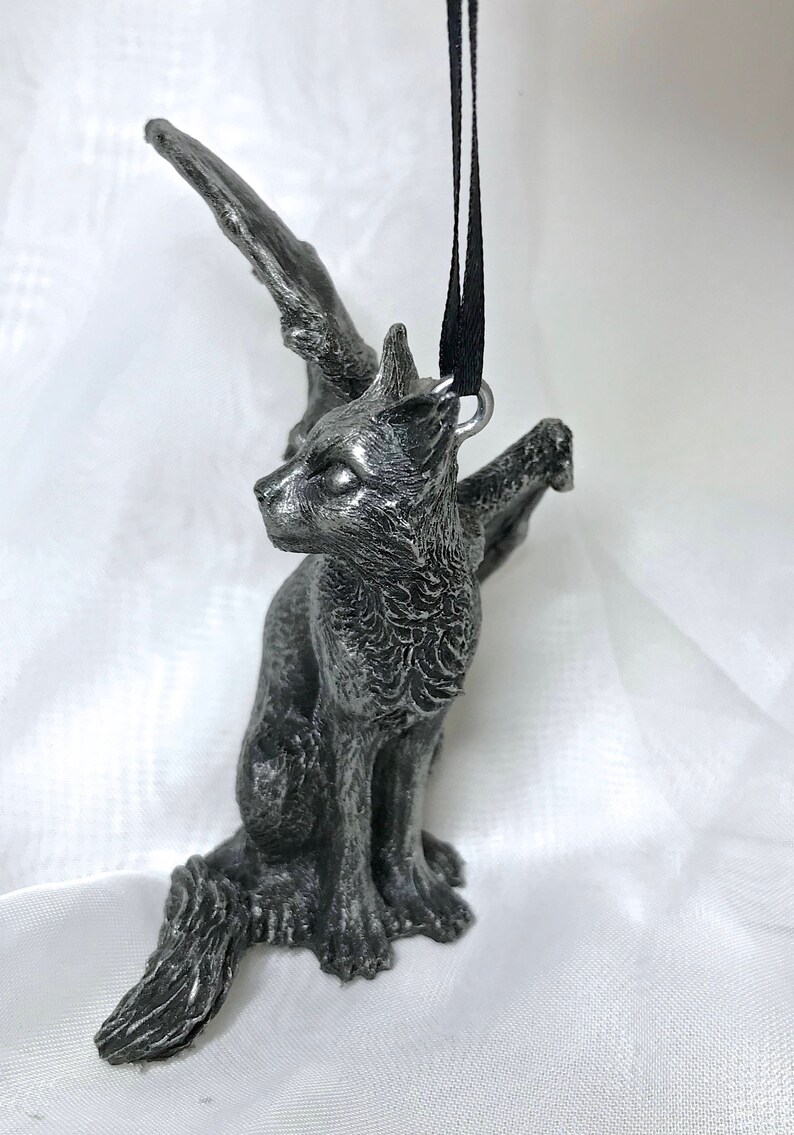May include: A silver-colored winged cat figurine ornament with a black ribbon attached to a loop on its back.
