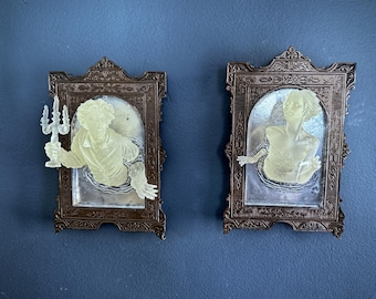 May include: Two ornate wooden frames with a ghostly figure inside each. The figures are translucent and appear to be floating in the frames. One figure holds a candelabra.