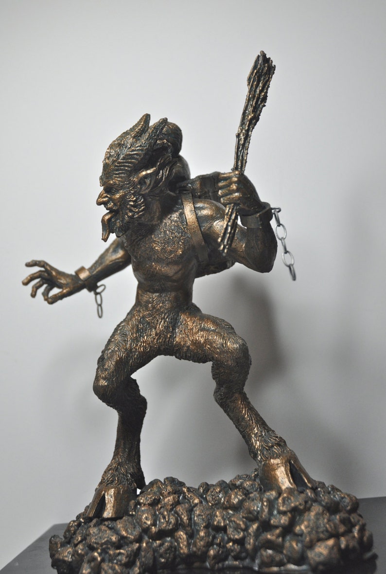 May include: A bronze statue of a goat-like creature with horns, a chain, and a stick in its hand. The creature is standing on a rocky base.