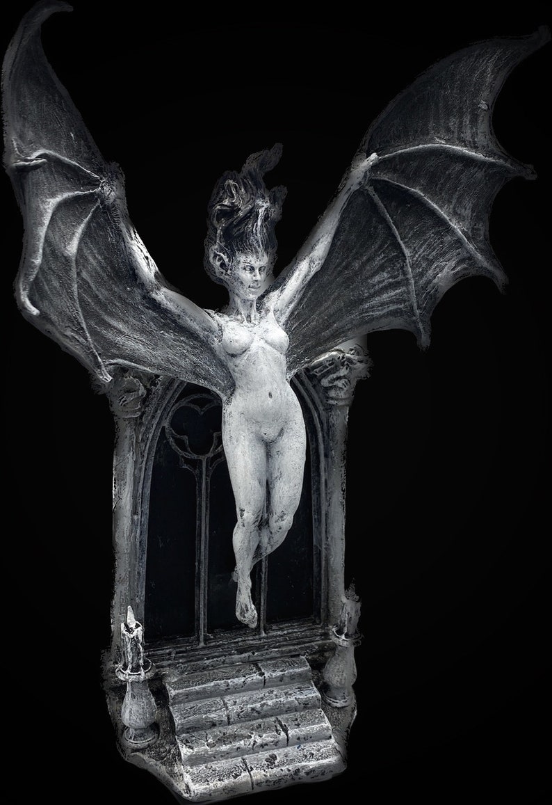 Pode incluir: Uma figura branca esculpida de uma mulher com asas, de p&eacute; em uma porta com arco pontiagudo. A figura est&aacute; nua e tem cabelo comprido e solto. A porta &eacute; decorada com uma janela de vitral e dois casti&ccedil;ais.