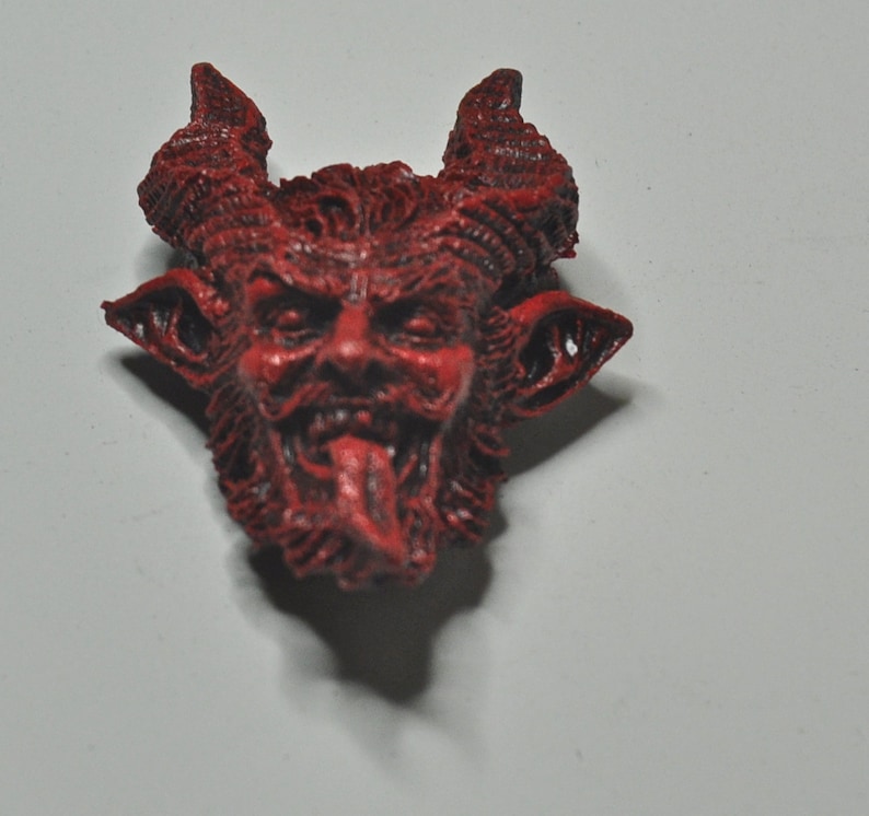 May include: A red, detailed, ceramic figurine of a devil with horns, a beard, and a protruding tongue.